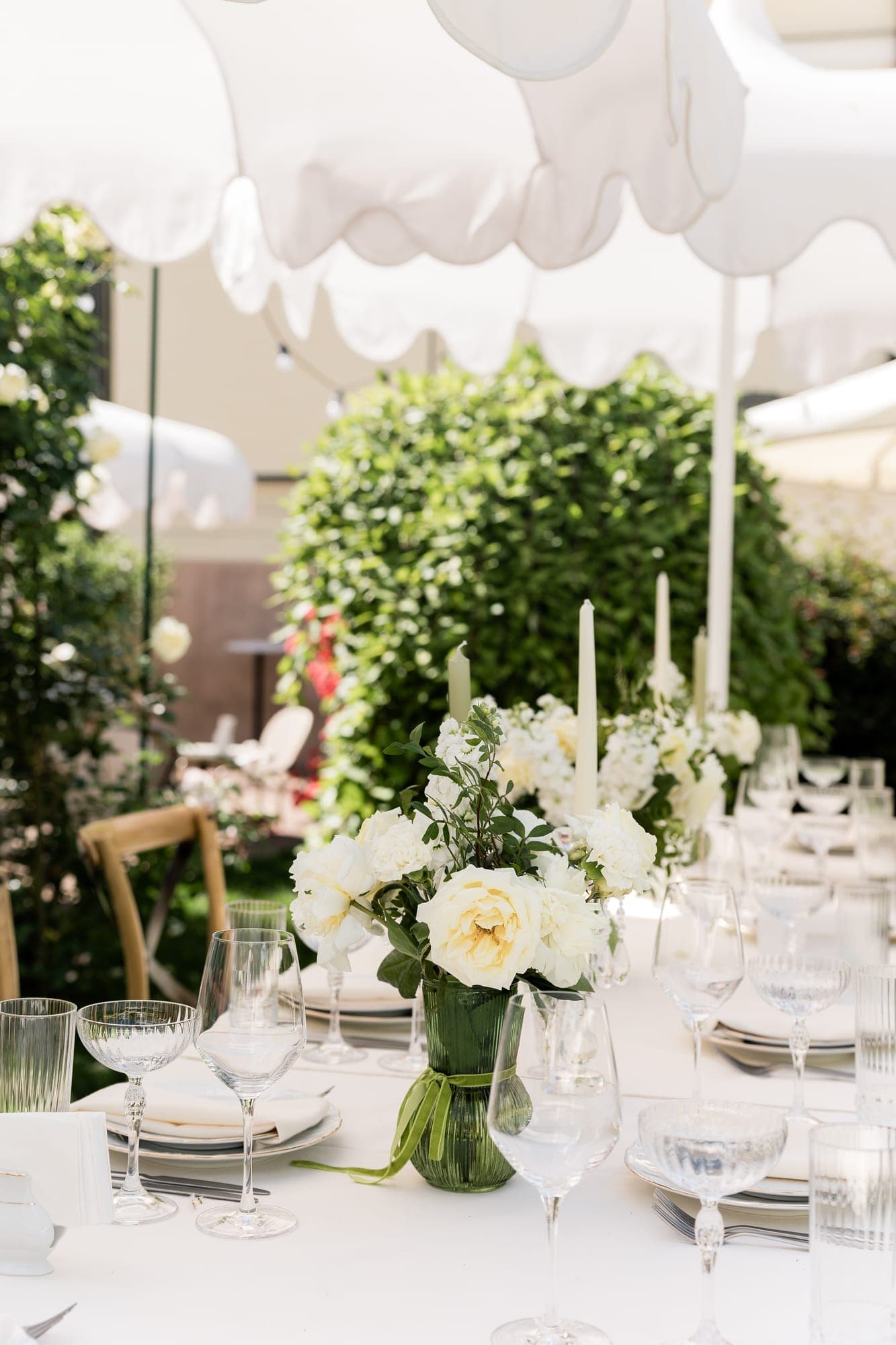 Gedeckte Hochzeitstafel mit weißen Blumen unter Sonnenschirmen