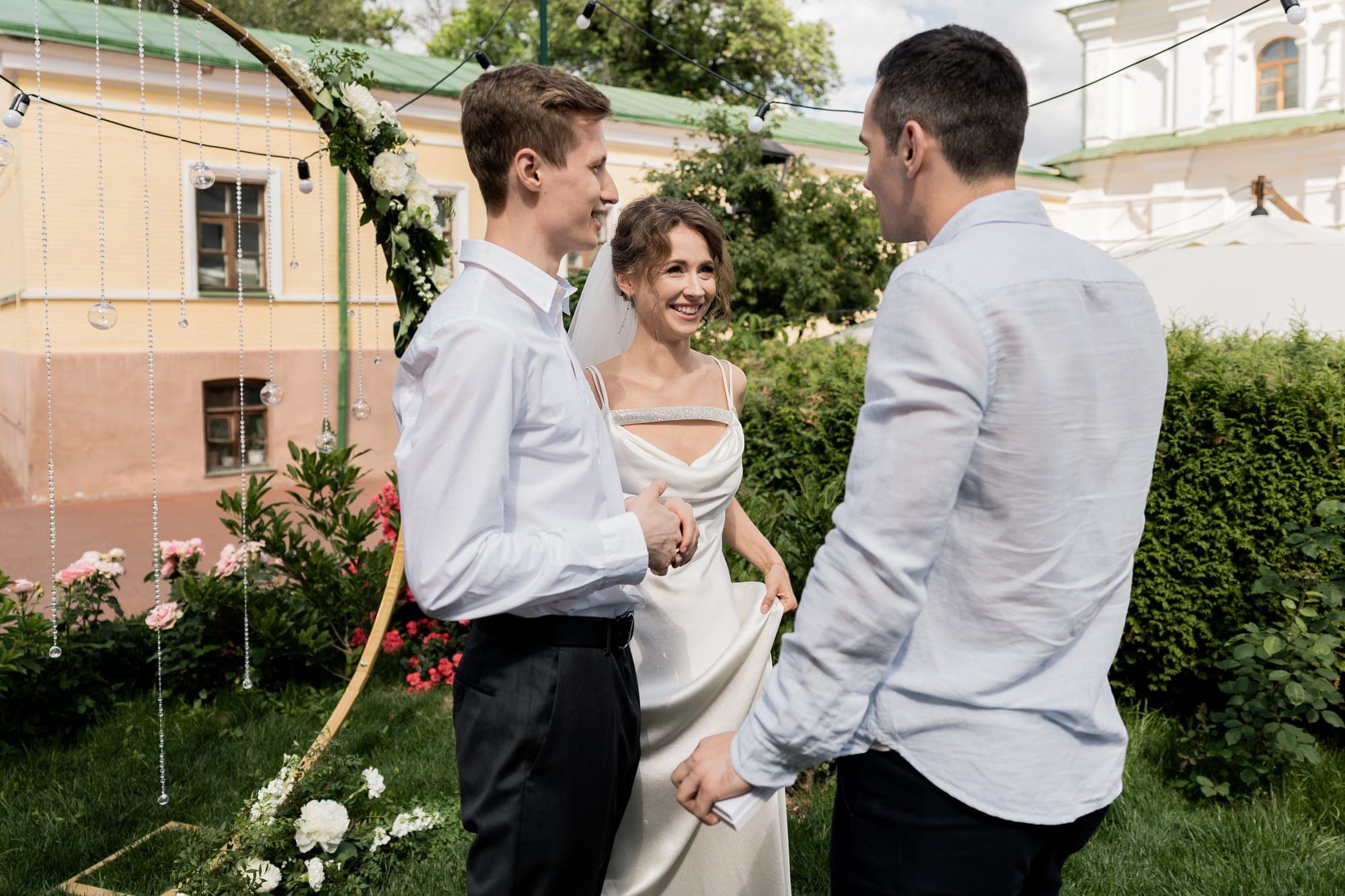 Das Brautpaar lacht während der Trauung unter dem Blumenbogen