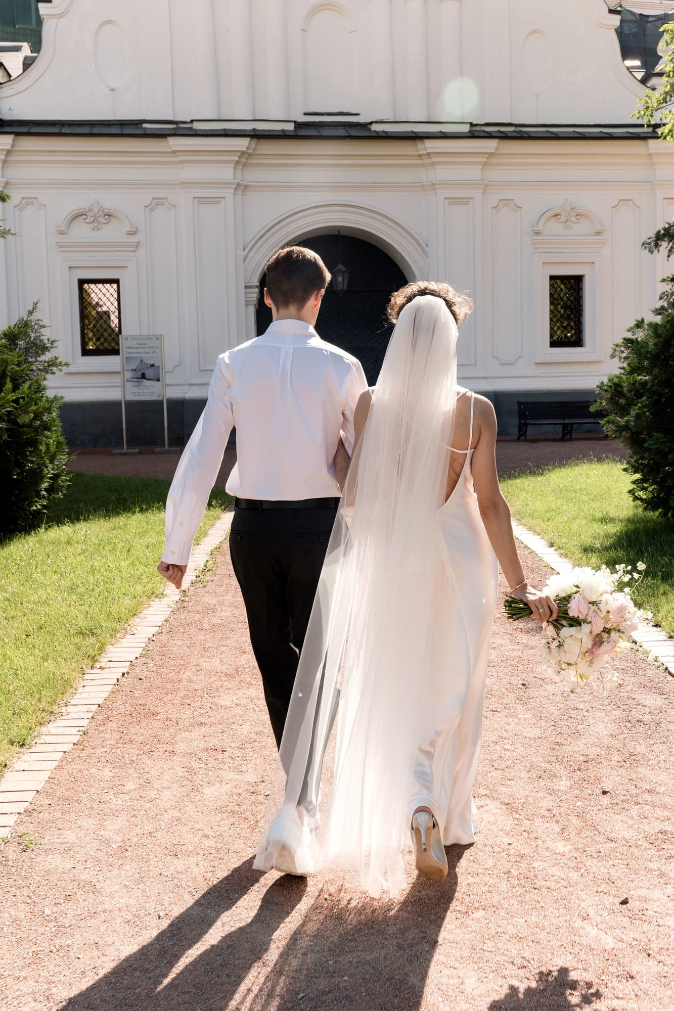 Brautpaar geht Hand in Hand auf eine Kirche zu