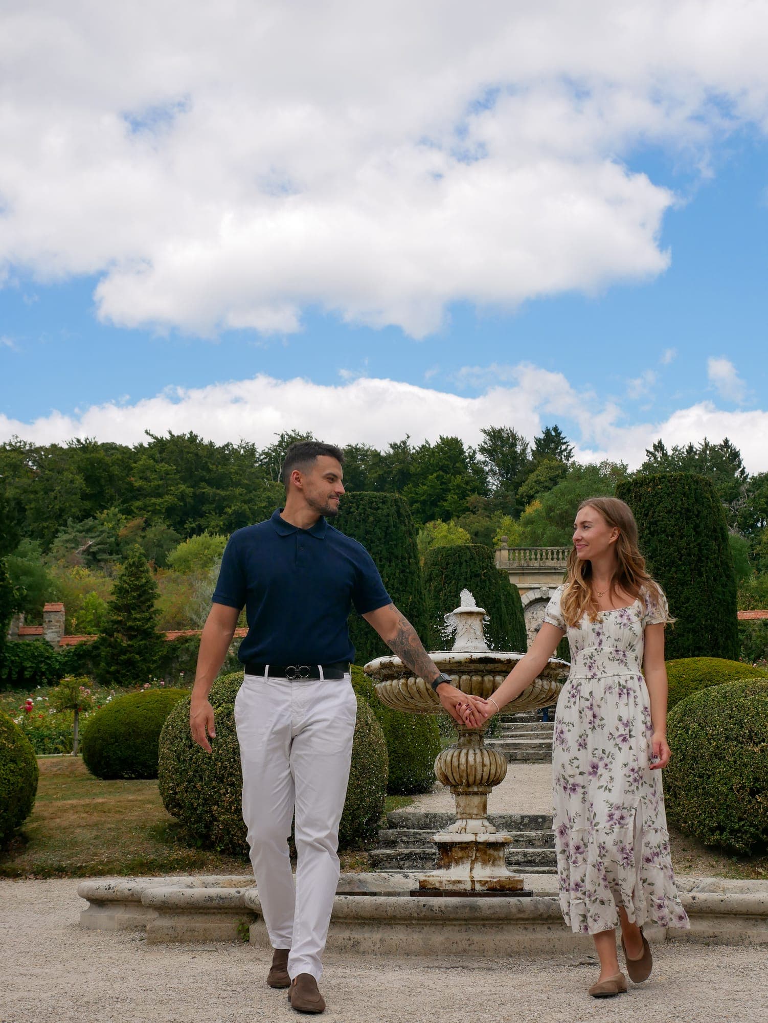 Paar spaziert Hand in Hand an einem Brunnen in einem Schlossgarten vorbei